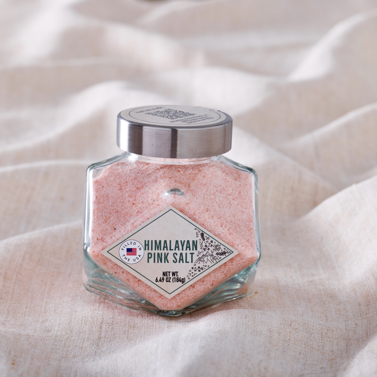 Himalayan pink salt in a clear glass jar with a silver metal cap