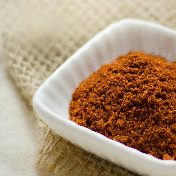 Bright orange red chili powder in a white square dish on a beige fabric and burlap background from the Spice Market collection